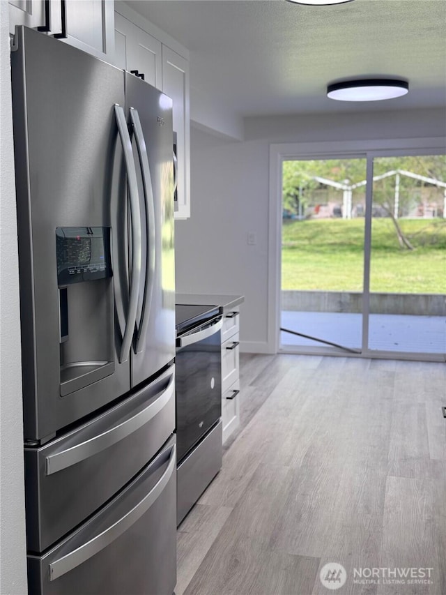 kitchen with stainless steel appliances, white cabinetry, and light wood-style floors