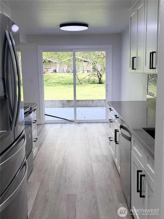 kitchen with white cabinets, appliances with stainless steel finishes, a healthy amount of sunlight, and light wood-type flooring