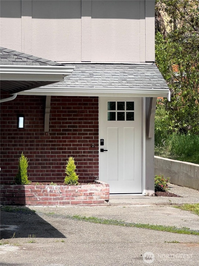 property entrance featuring roof with shingles and brick siding
