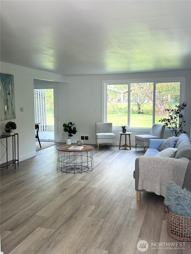 living room featuring visible vents, baseboards, wood finished floors, and a wealth of natural light