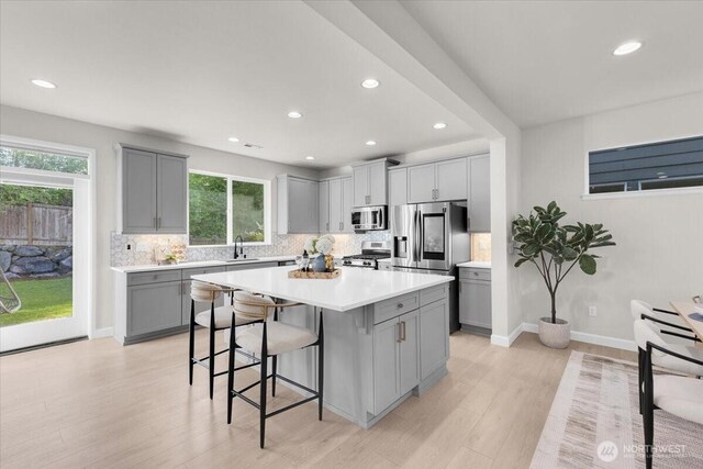 kitchen featuring gray cabinetry, backsplash, stainless steel appliances, and a kitchen bar