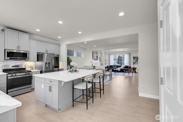 kitchen featuring a breakfast bar, light countertops, tasteful backsplash, light wood finished floors, and appliances with stainless steel finishes