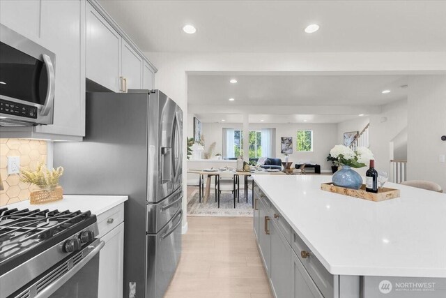 kitchen with gray cabinetry, light countertops, stainless steel microwave, recessed lighting, and gas range oven