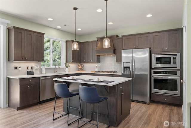 kitchen with appliances with stainless steel finishes, premium range hood, a sink, dark brown cabinetry, and a center island