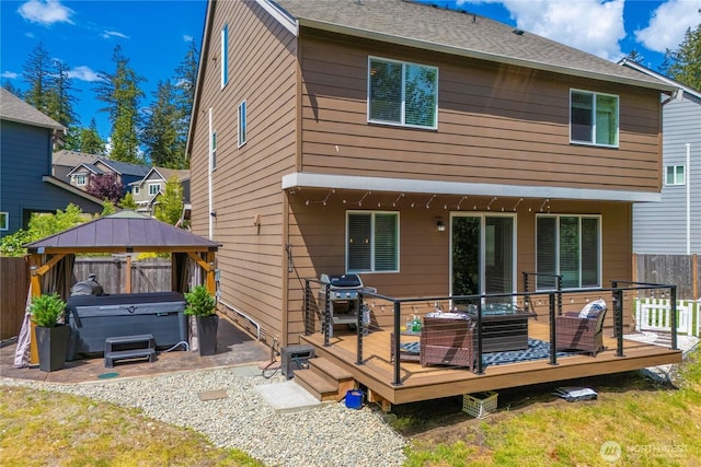 back of property with a hot tub, a wooden deck, a gazebo, a fenced backyard, and a patio