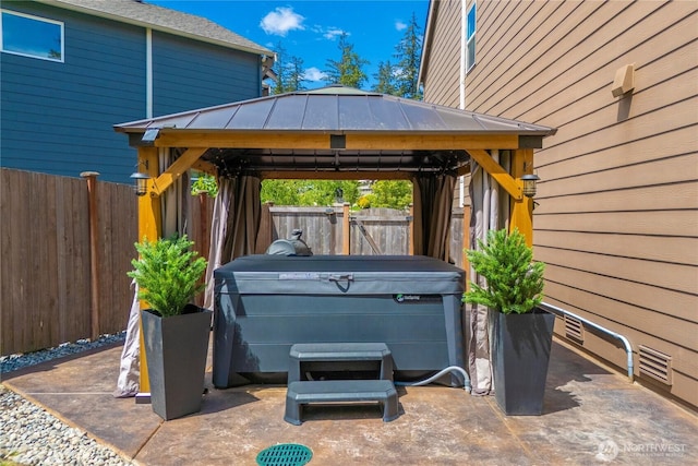 view of patio with a hot tub, a gazebo, and fence