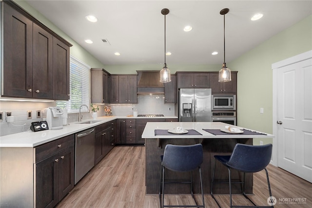 kitchen with appliances with stainless steel finishes, a sink, custom exhaust hood, dark brown cabinetry, and light wood-type flooring