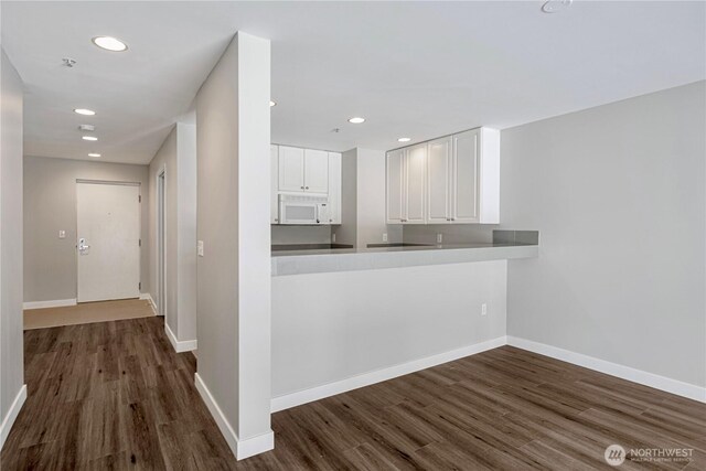 kitchen featuring baseboards, white cabinets, white microwave, and dark wood-style floors