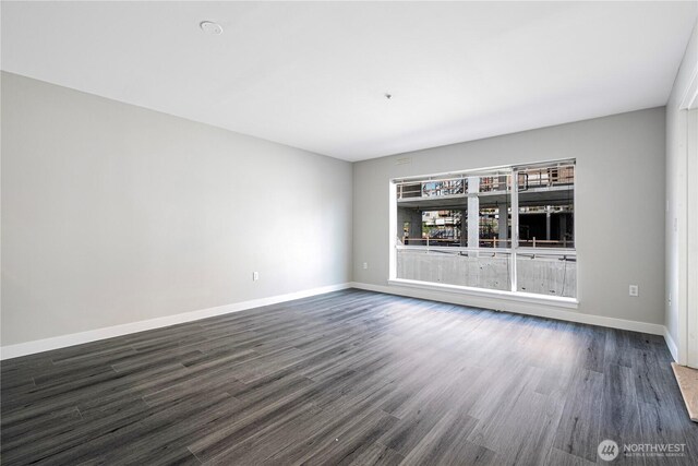 spare room with baseboards and dark wood-style flooring