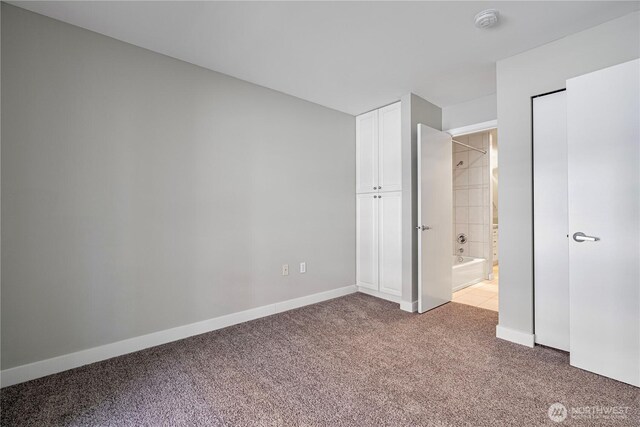 unfurnished bedroom with carpet flooring, baseboards, and ensuite bath