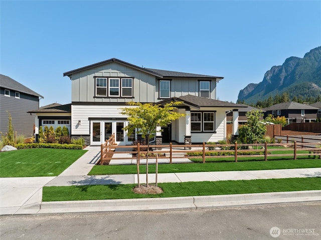 view of front facade with board and batten siding, a mountain view, french doors, and a fenced front yard