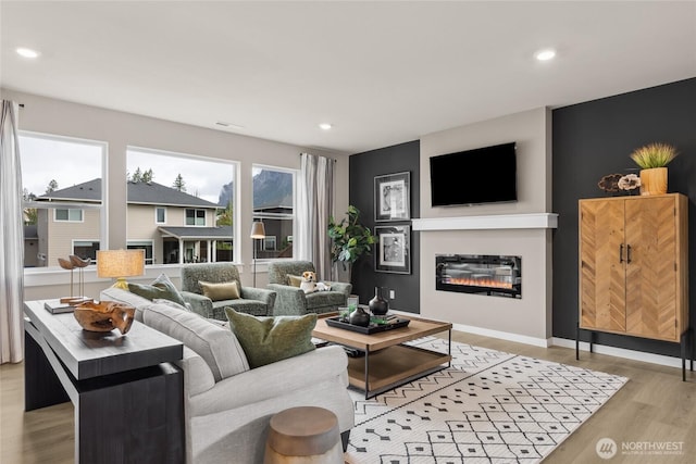 living room featuring recessed lighting, a glass covered fireplace, and light wood-type flooring