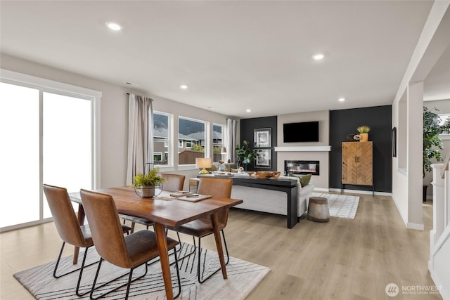 dining space featuring recessed lighting, a glass covered fireplace, and light wood-type flooring