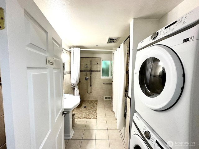 washroom featuring laundry area, visible vents, tile walls, stacked washing maching and dryer, and light tile patterned floors