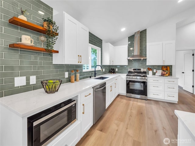 kitchen with appliances with stainless steel finishes, a sink, wall chimney exhaust hood, lofted ceiling, and tasteful backsplash