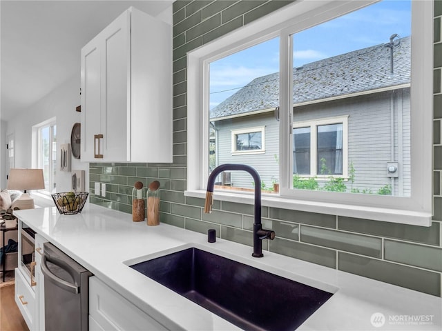 kitchen featuring a sink, white cabinets, stainless steel dishwasher, and backsplash