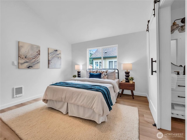 bedroom featuring heating unit, light wood-style floors, baseboards, a barn door, and vaulted ceiling