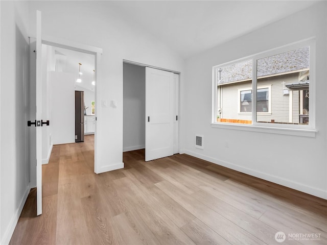 unfurnished bedroom featuring baseboards, vaulted ceiling, and light wood-style floors