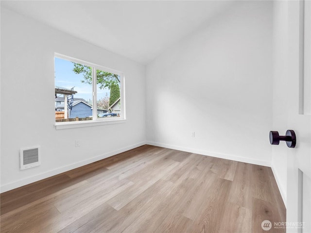 empty room with baseboards, vaulted ceiling, wood finished floors, and visible vents