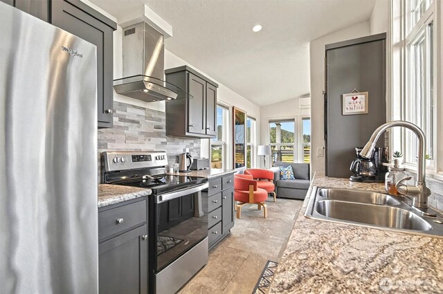 kitchen with decorative backsplash, a sink, lofted ceiling, stainless steel appliances, and wall chimney exhaust hood