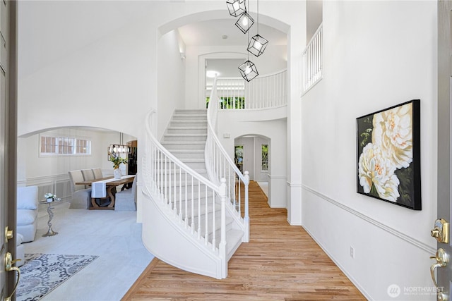 staircase featuring a high ceiling, arched walkways, wood finished floors, and a chandelier