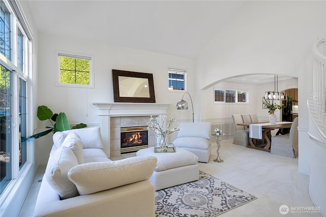 carpeted living area with high vaulted ceiling, a chandelier, a tiled fireplace, and arched walkways
