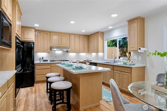 kitchen with light brown cabinetry, under cabinet range hood, black appliances, a center island, and light wood-style floors