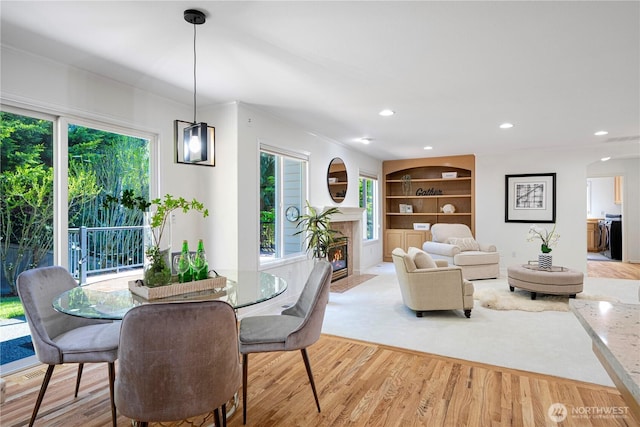 dining space with a fireplace with flush hearth, built in features, wood finished floors, recessed lighting, and arched walkways