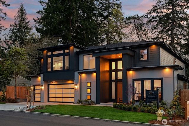 modern home with a lawn, a garage, fence, concrete driveway, and stucco siding