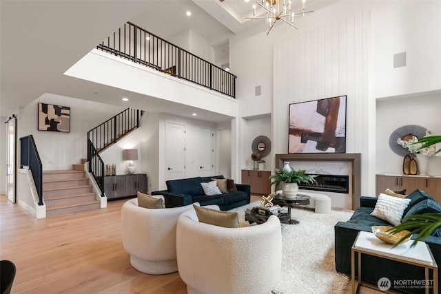 living area with a towering ceiling, a fireplace, stairway, a notable chandelier, and light wood-style floors