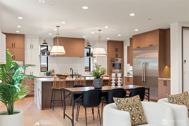 kitchen with brown cabinetry, a kitchen island with sink, recessed lighting, light countertops, and stainless steel appliances