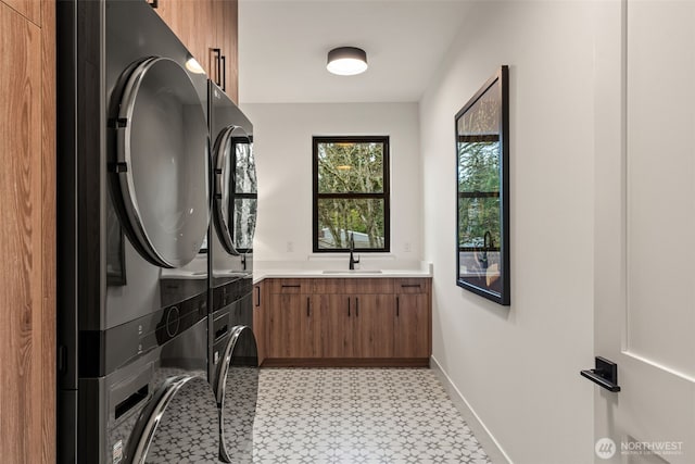 washroom featuring stacked washer and dryer, cabinet space, a sink, baseboards, and light floors