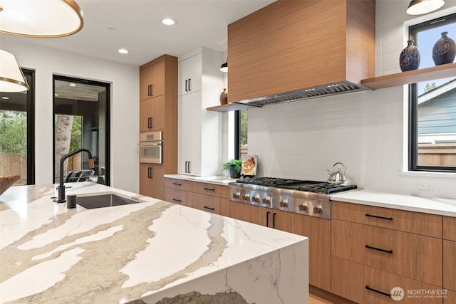 kitchen featuring light stone countertops, appliances with stainless steel finishes, a sink, premium range hood, and tasteful backsplash