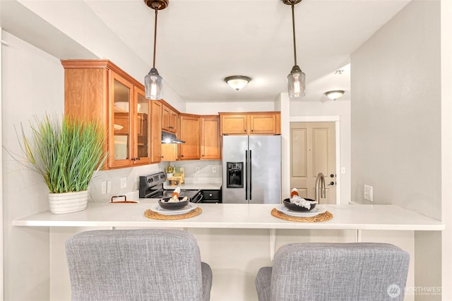 kitchen with a peninsula, glass insert cabinets, under cabinet range hood, decorative light fixtures, and stainless steel appliances