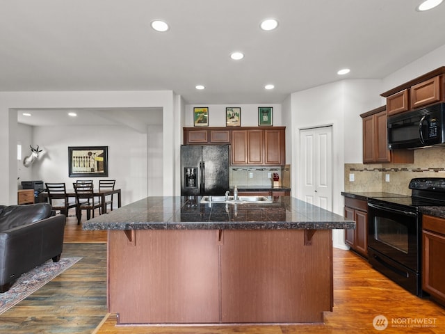 kitchen featuring black appliances, a breakfast bar, dark wood-style floors, tile countertops, and backsplash