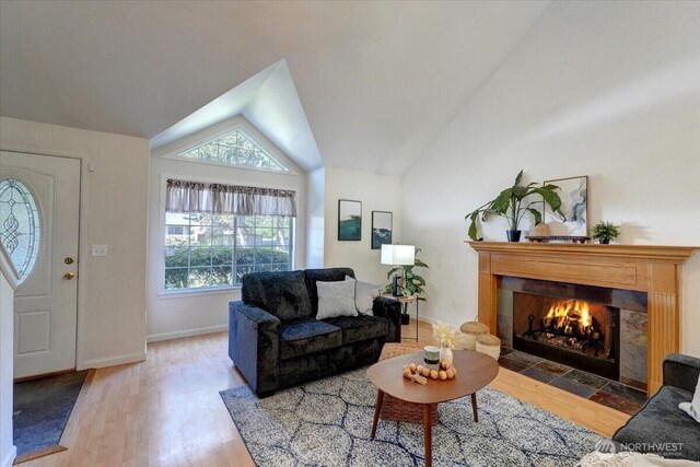 living area with vaulted ceiling, healthy amount of natural light, wood finished floors, a tile fireplace, and baseboards