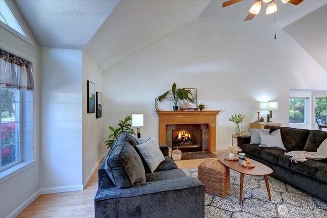 living area featuring lofted ceiling, a fireplace with flush hearth, a ceiling fan, light wood-style floors, and baseboards