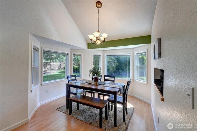 dining room with a textured wall, a chandelier, light wood-style floors, lofted ceiling, and baseboards