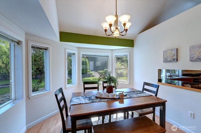 dining area featuring baseboards, light wood finished floors, lofted ceiling, a chandelier, and a textured wall