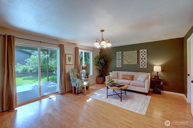 living room featuring a chandelier, light wood-style flooring, baseboards, and a textured ceiling