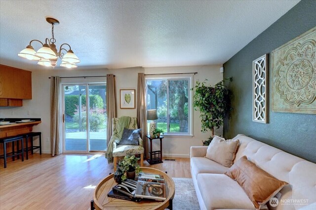 living area with a textured ceiling, light wood-style floors, a chandelier, and baseboards
