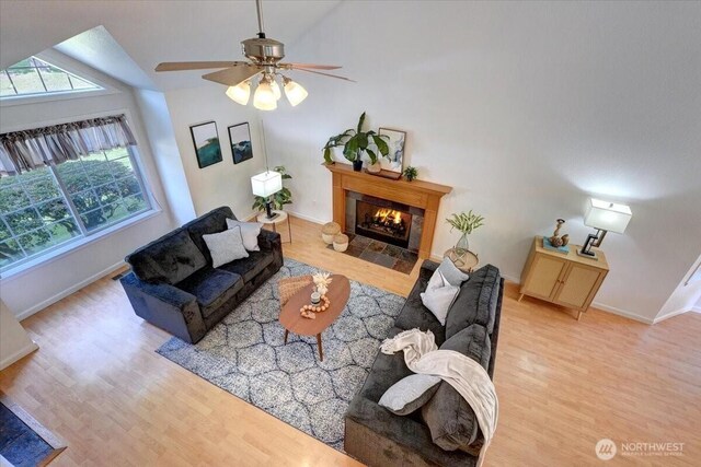 living room featuring wood finished floors, a fireplace, baseboards, vaulted ceiling, and ceiling fan