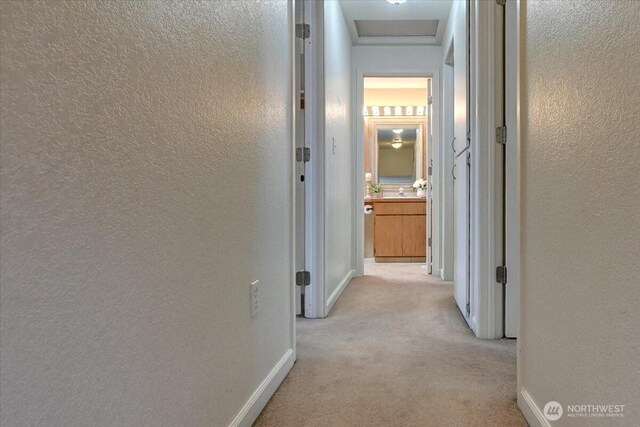 hall with a textured wall, light colored carpet, and baseboards