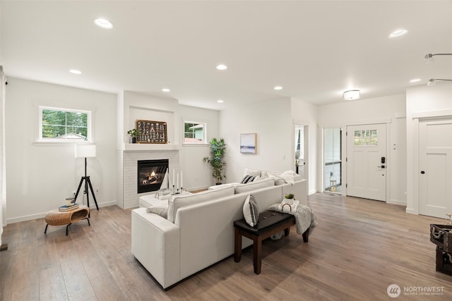 living room featuring a brick fireplace, recessed lighting, a healthy amount of sunlight, and light wood-type flooring