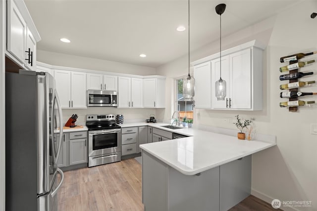 kitchen featuring a sink, gray cabinets, light wood-style flooring, stainless steel appliances, and a peninsula