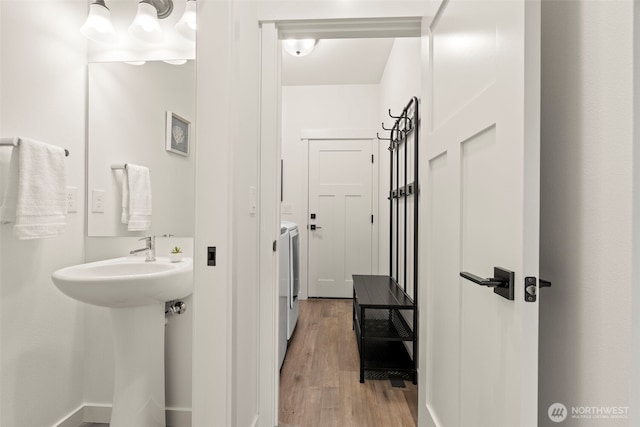 bathroom featuring wood finished floors, a sink, baseboards, and washing machine and dryer