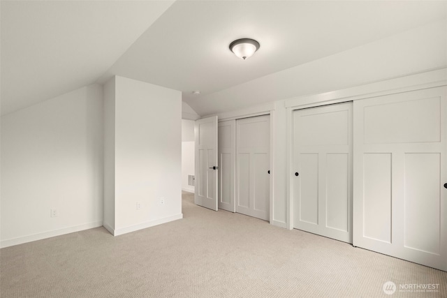 unfurnished bedroom featuring baseboards, two closets, light colored carpet, and lofted ceiling