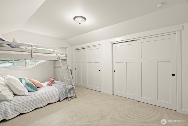 bedroom with light colored carpet, lofted ceiling, and two closets