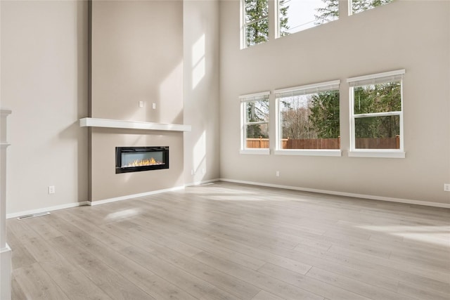 unfurnished living room with baseboards, a glass covered fireplace, wood finished floors, and a healthy amount of sunlight