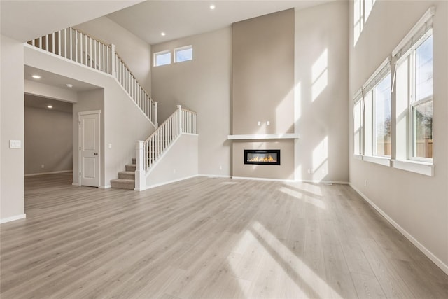 unfurnished living room with a glass covered fireplace, baseboards, a high ceiling, and wood finished floors